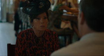 Movie still from “Confess, Fletch” (2022), directed by Greg Mottola – A woman wearing a hat sitting at a table in a restaurant; Close Up shot, Over the shoulder angle