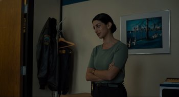 Movie still from “Confess, Fletch” (2022), directed by Greg Mottola – A woman standing with her arms crossed in front of a coat rack; Medium shot, Over the shoulder angle