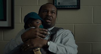 Movie still from “Confess, Fletch” (2022), directed by Greg Mottola – A man holding a baby in his arms; Close Up shot, Over the shoulder angle