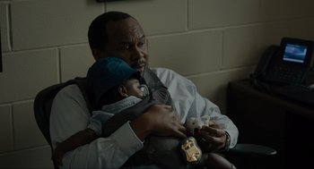 Movie still from “Confess, Fletch” (2022), directed by Greg Mottola – A man holding a baby in his arms; Close Up shot, High angle