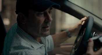 Movie still from “Confess, Fletch” (2022), directed by Greg Mottola – A person driving a car wearing a hat; Close Up shot, Over the shoulder angle