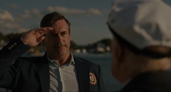 Movie still from “Confess, Fletch” (2022), directed by Greg Mottola – A man saluting another man wearing a sailor's hat; Medium shot, Low angle