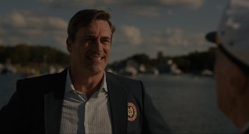 Movie still from “Confess, Fletch” (2022), directed by Greg Mottola – A man in a suit smiling for the camera; Close Up shot, Over the shoulder angle