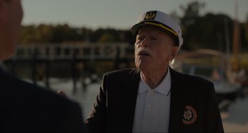 Movie still from “Confess, Fletch” (2022), directed by Greg Mottola – An older man wearing a hat and a suit; Close Up shot, Over the shoulder angle