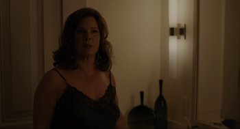 Movie still from “Confess, Fletch” (2022), directed by Greg Mottola – A woman standing in a dark room with a wine bottle; Medium shot, Over the shoulder angle