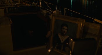 Movie still from “Confess, Fletch” (2022), directed by Greg Mottola – A person holding a painting in a dark room; Close Up shot, Over the shoulder angle