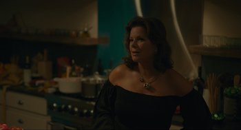 Movie still from “Confess, Fletch” (2022), directed by Greg Mottola – A woman in a black dress is standing in a kitchen; Medium shot, Over the shoulder angle