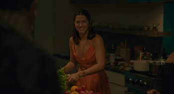 Movie still from “Confess, Fletch” (2022), directed by Greg Mottola – A woman in an orange dress cutting vegetables; Medium shot, Over the shoulder angle