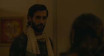 Movie still from “Confess, Fletch” (2022), directed by Greg Mottola – A man wearing a scarf looking into a mirror; Close Up shot, Over the shoulder angle