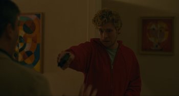 Movie still from “Confess, Fletch” (2022), directed by Greg Mottola – A man in a red jacket holding a remote control; Medium shot, Over the shoulder angle