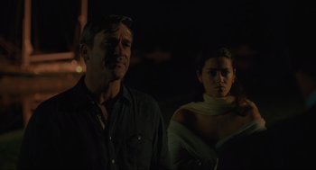 Movie still from “Confess, Fletch” (2022), directed by Greg Mottola – A man and a woman standing next to each other in the dark; Medium shot, Over the shoulder angle