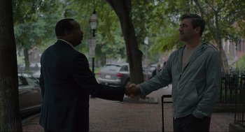 Movie still from “Confess, Fletch” (2022), directed by Greg Mottola – Two men are shaking hands on the sidewalk; Medium shot, Over the shoulder angle