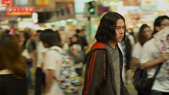 Movie still from “Contagion” (2011), directed by Steven Soderbergh – A man with long black hair walking down a street; Medium shot, Low angle