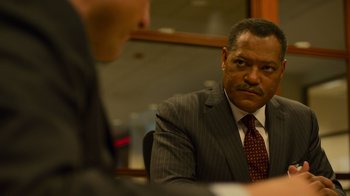 Movie still from “Contagion” (2011), directed by Steven Soderbergh – A man wearing a suit and tie sitting at a table; Close Up shot, Over the shoulder angle