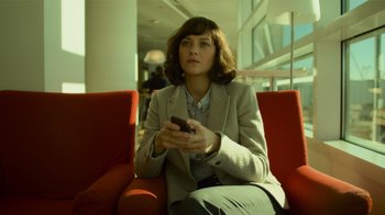 Movie still from “Contagion” (2011), directed by Steven Soderbergh – A woman sitting on a red couch holding a cell phone; Medium shot, High angle
