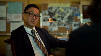 Movie still from “Contagion” (2011), directed by Steven Soderbergh – A man wearing a suit and tie sitting in a chair; Close Up shot, Over the shoulder angle