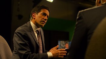 Movie still from “Contagion” (2011), directed by Steven Soderbergh – A man wearing a suit and tie talking to someone; Medium shot, Over the shoulder angle