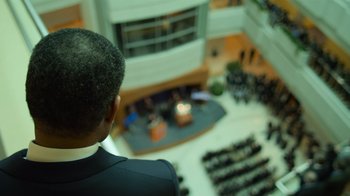 Movie still from “Contagion” (2011), directed by Steven Soderbergh – A man standing in front of an audience in an auditorium; Extreme Close Up shot, Over the shoulder angle