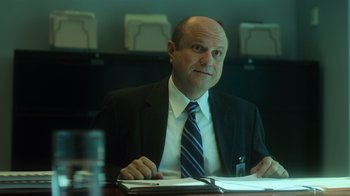 Movie still from “Contagion” (2011), directed by Steven Soderbergh – A man sitting at a table in front of papers; Medium shot, Over the shoulder angle