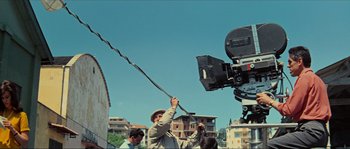Movie still from “Contempt” (1963), directed by Jean-Luc Godard – A man is holding a video camera up to the camera; Wide shot, Low angle