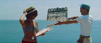 Movie still from “Contempt” (1963), directed by Jean-Luc Godard – A woman in a bikini holding a clapperboard in front of the ocean; Medium shot, Low angle