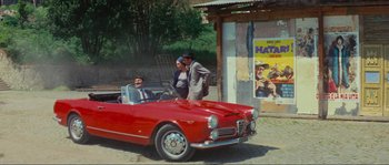 Movie still from “Contempt” (1963), directed by Jean-Luc Godard – Two men standing in the back seat of a red car; Wide shot, High angle