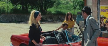 Movie still from “Contempt” (1963), directed by Jean-Luc Godard – Two women and a man riding in the back of a red car; Medium shot, High angle