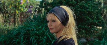 Movie still from “Contempt” (1963), directed by Jean-Luc Godard – A woman wearing a black head band in front of some bushes; Close Up shot, Low angle