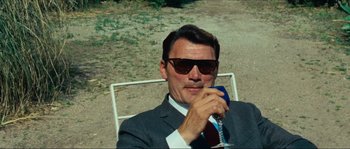 Movie still from “Contempt” (1963), directed by Jean-Luc Godard – A man in a suit and sunglasses sitting in a chair; Medium shot, Low angle