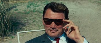 Movie still from “Contempt” (1963), directed by Jean-Luc Godard – A person wearing a suit and sunglasses; Close Up shot, Low angle