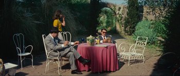 Movie still from “Contempt” (1963), directed by Jean-Luc Godard – Two men and a woman sitting at a table outside; Wide shot, High angle