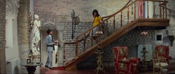 Movie still from “Contempt” (1963), directed by Jean-Luc Godard – A woman talking on a phone while standing on a staircase; Wide shot, High angle