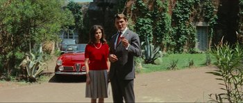 Movie still from “Contempt” (1963), directed by Jean-Luc Godard – A man and a woman standing next to each other in front of a car; Medium shot, Low angle