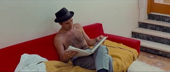 Movie still from “Contempt” (1963), directed by Jean-Luc Godard – A man sitting on a couch reading a book; Medium shot, High angle
