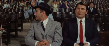 Movie still from “Contempt” (1963), directed by Jean-Luc Godard – Two men in suits and hats sitting next to each other in front of an audience; Medium shot, High angle