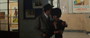 Movie still from “Contempt” (1963), directed by Jean-Luc Godard – A man and a woman kissing in front of a movie poster; Medium shot, Over the shoulder angle