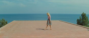 Movie still from “Contempt” (1963), directed by Jean-Luc Godard – A woman walking on a brick path near the ocean; Wide shot, High angle