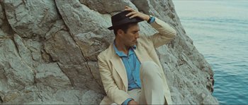 Movie still from “Contempt” (1963), directed by Jean-Luc Godard – A man sitting on the ground wearing a suit and a hat; Medium shot, Low angle