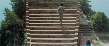Movie still from “Contempt” (1963), directed by Jean-Luc Godard – A man in a suit walking up a set of stairs; Extreme Wide shot, High angle