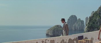 Movie still from “Contempt” (1963), directed by Jean-Luc Godard – A man in a suit and hat standing on a ledge; Wide shot, Low angle