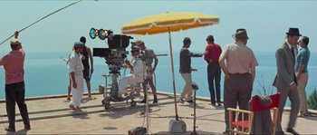 Movie still from “Contempt” (1963), directed by Jean-Luc Godard – A group of people standing under a yellow umbrella; Wide shot, High angle