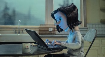 Movie still from “Coraline” (2009), directed by Henry Selick – A doll is sitting at a table and using a laptop computer; Medium shot, Over the shoulder angle