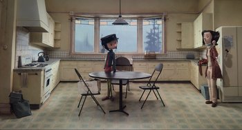 Movie still from “Coraline” (2009), directed by Henry Selick – A doll sitting at a round table in a kitchen; Wide shot, High angle