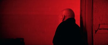 Movie still from “Cosmic Sin” (2021), directed by Edward Drake – A man with a bald head standing in front of a red wall; Medium shot, Low angle