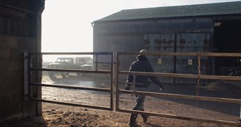 Movie still from “Cow” (2021), directed by Andrea Arnold – A man walking through a gate on a dirt field; Wide shot, Low angle