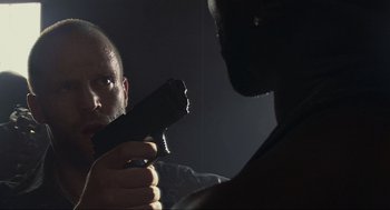 Movie still from “Crank” (2006), directed by Mark Neveldine – A man holding a gun in front of another man; Close Up shot, Low angle