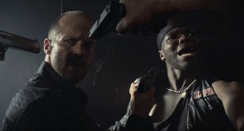 Movie still from “Crank” (2006), directed by Mark Neveldine – Two men are holding guns in a dark room; Close Up shot, Low angle