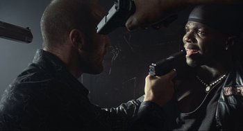 Movie still from “Crank” (2006), directed by Mark Neveldine – A man holding a gun pointed at another man with a gun; Close Up shot, Low angle