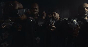 Movie still from “Crank” (2006), directed by Mark Neveldine – A group of men standing next to each other in a dark room; Medium shot, Low angle