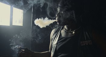 Movie still from “Crank” (2006), directed by Mark Neveldine – A man is smoking a cigarette in a dark room; Medium shot, Low angle